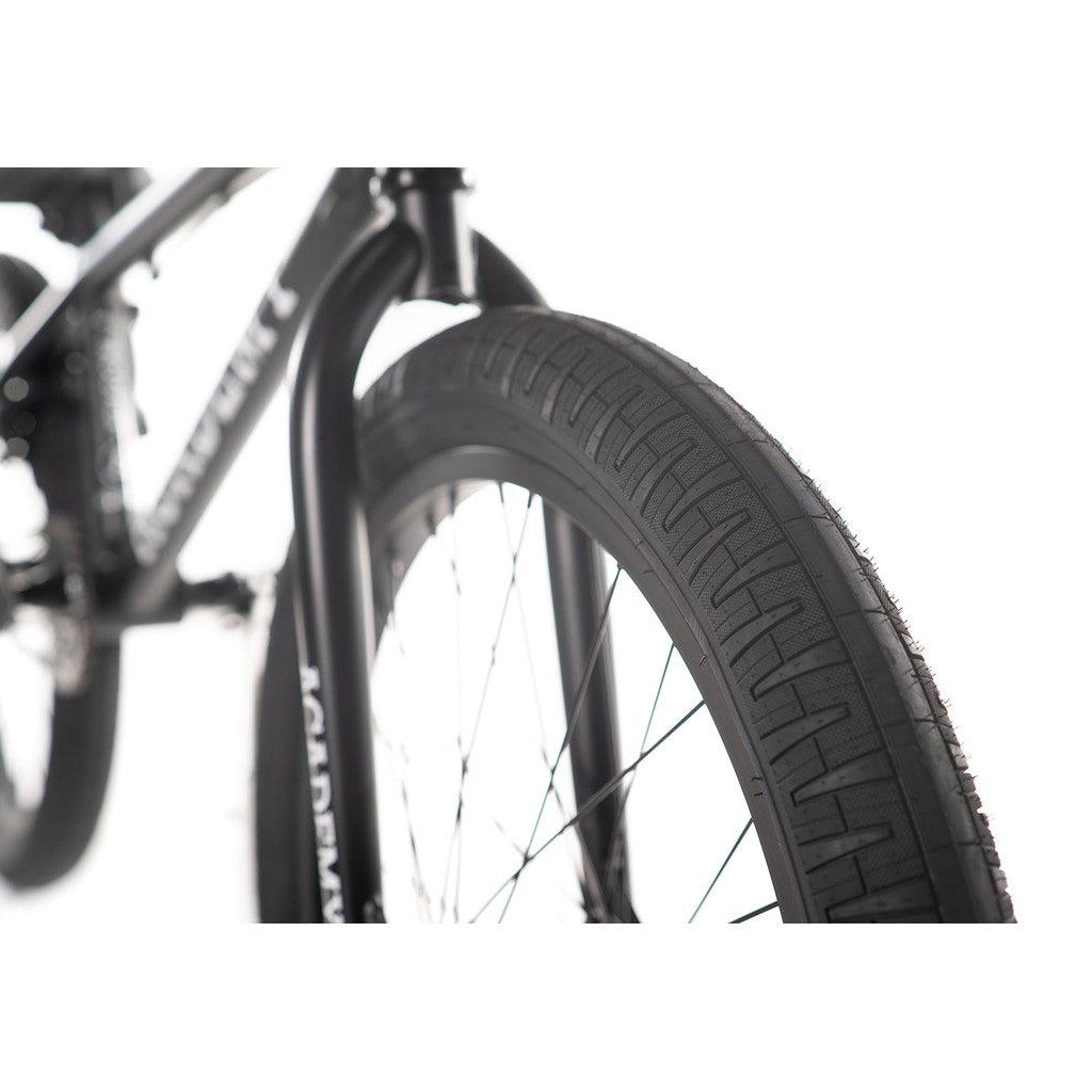 A close-up of a front wheel with a distinct tire tread pattern highlights the sturdy design of the Academy Trooper 20 Inch Bike, featuring its Hi-Ten steel frame and efficient sealed hubs, all set against a pristine white background.