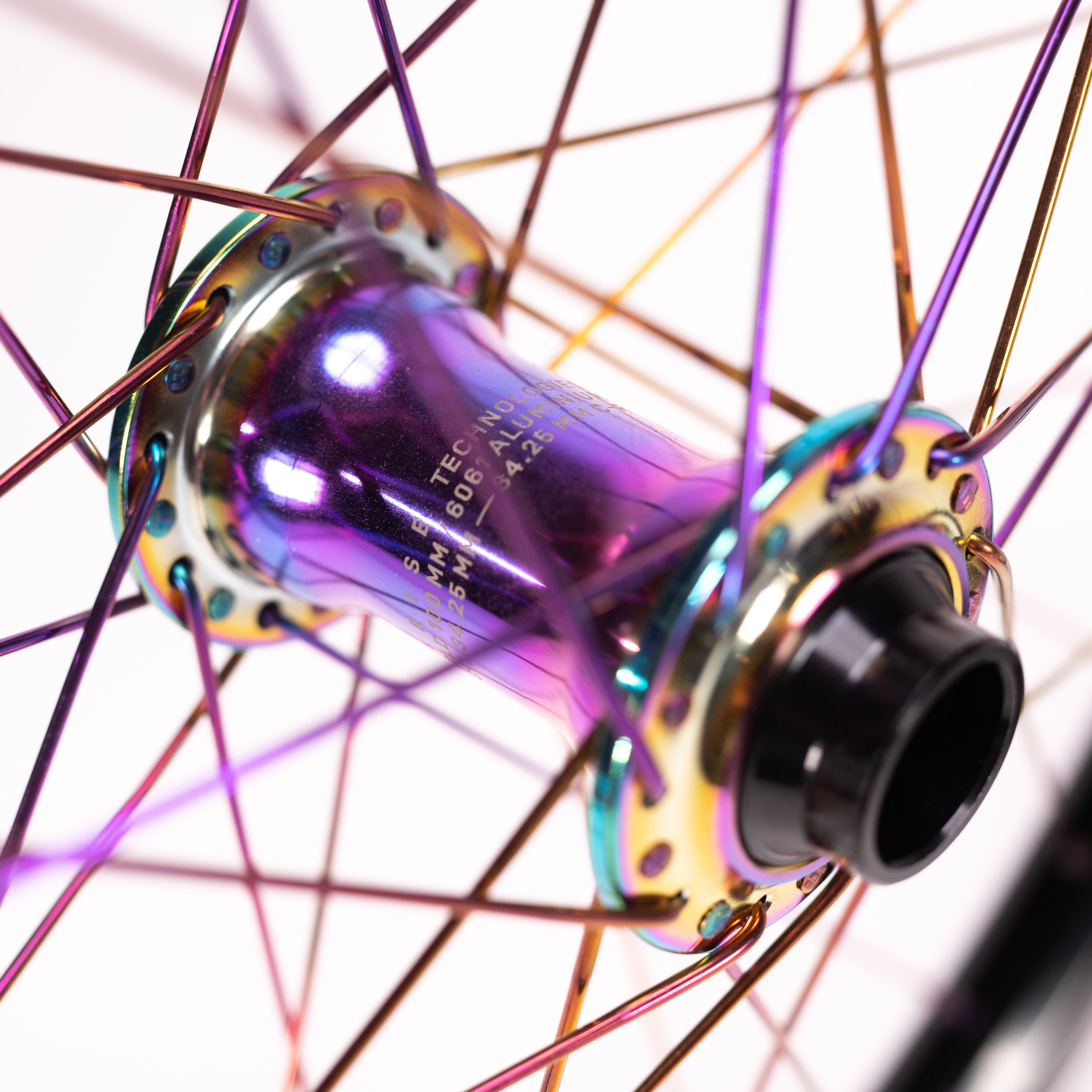 A close-up of the Arise Echo Oilslick Pro 20 Inch Wheelset hub reveals iridescent colors and radiating spokes. The metal's vibrant spectrum is enhanced by its high engagement drive, forming a captivating pattern.