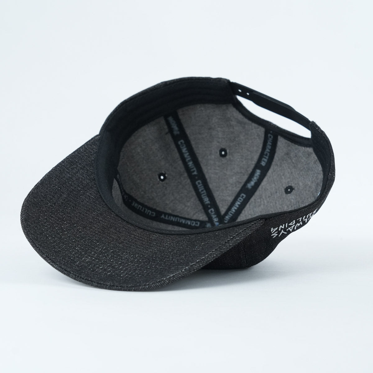 The Backbone Always Building Hat is a black unstructured 5-panel cap with an inner lining, ventilation eyelets, and an adjustable back strap, shown here from underneath.