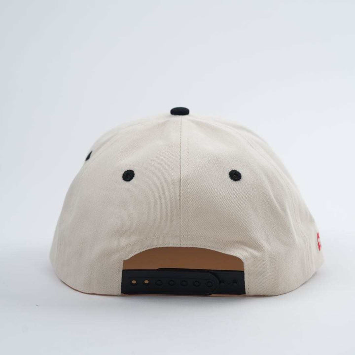 Back view of the Backbone Always Building Hat, an unstructured beige baseball cap featuring a black adjustable strap, black top dot, and embroidered logo.