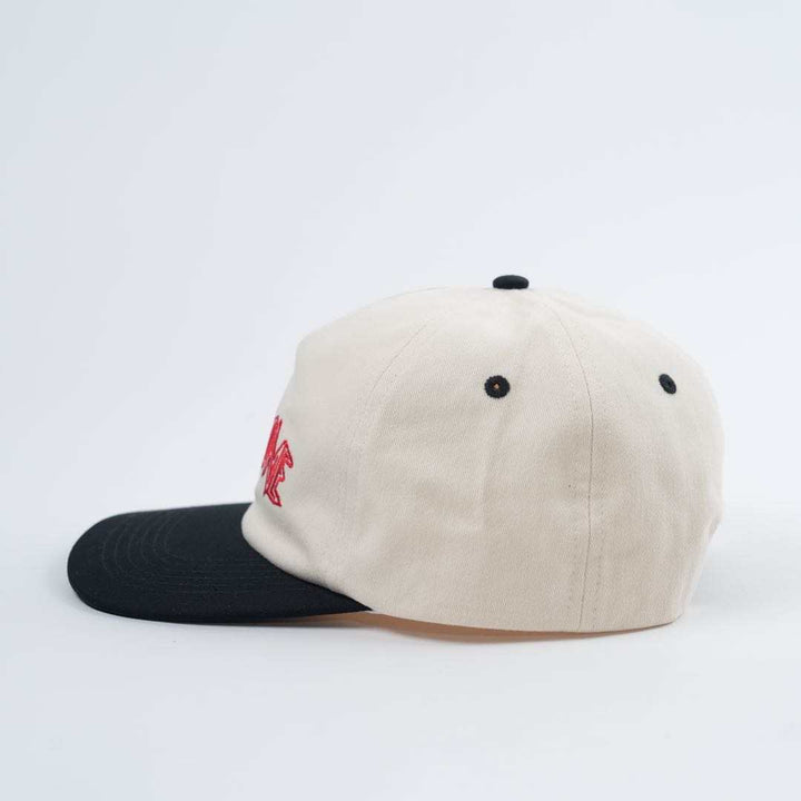 The Backbone Always Building Hat features a two-tone design with a beige crown and black brim, complete with a red embroidered logo. This unstructured baseball cap is perfect for casual outings and ideal for Backbone BMX enthusiasts.