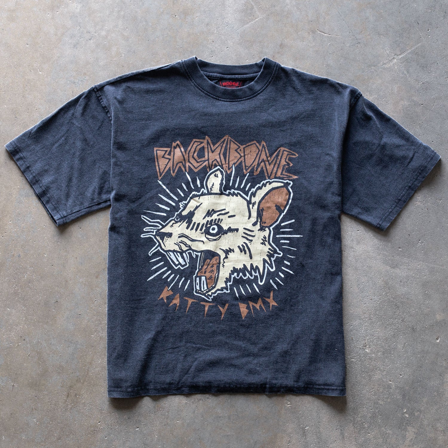 The Backbone Ratty BMX T-Shirt is a vintage-style black tee made from premium cotton, featuring a stylized graphic of a snarling rat head with "BACKBONE" above and "RATTY DAY" below.