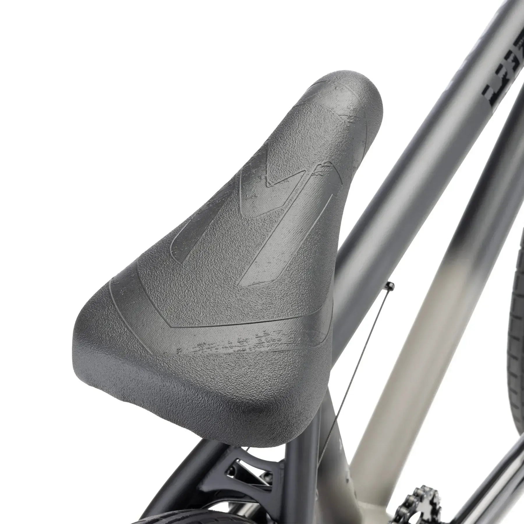 Close-up of a black seat on the Kink Curb 20 Inch Bike (2026), shown attached to the frame with part of the rear wheel and pedal visible—perfect for beginners or entry-level BMX riders.