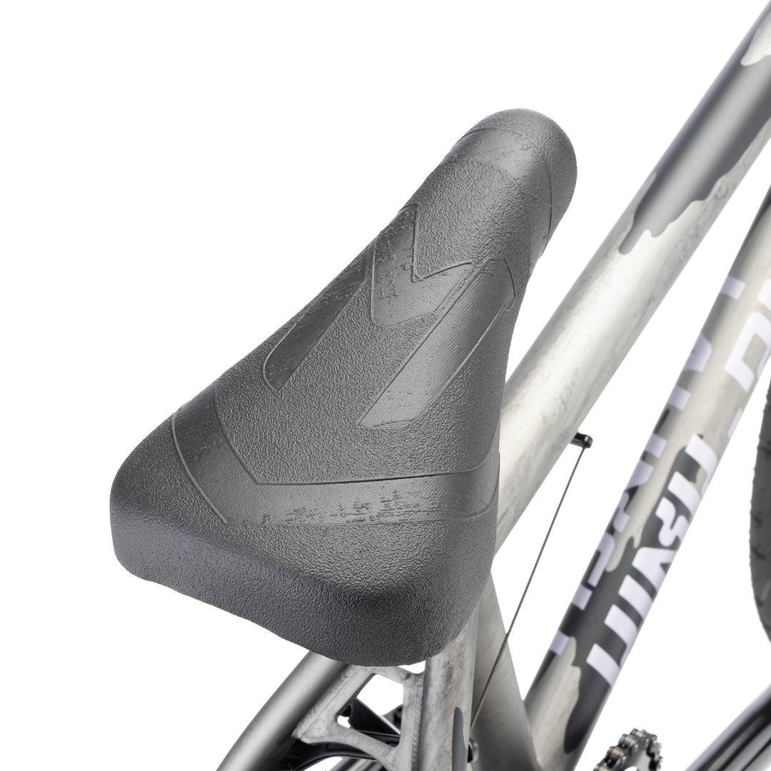 Close-up of the Kink Launch LTD 20 Inch Bike’s black BMX seat on a silver frame, with pedals and chain visible—ideal for showcasing this limited edition ride.