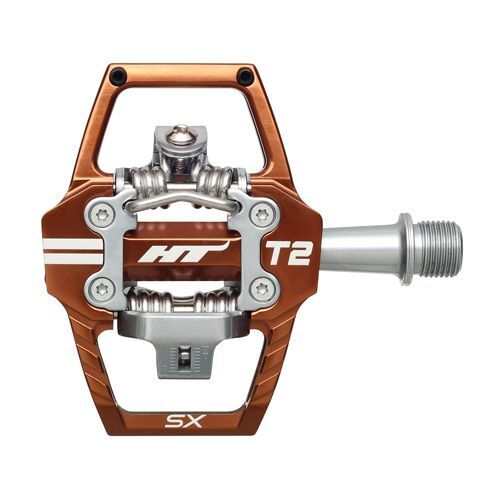 Close-up of the orange and silver HT T2-SX Clip In Pedals, highlighting their clipless binding mechanism and CNC machined chromoly spindle threading for secure attachment.