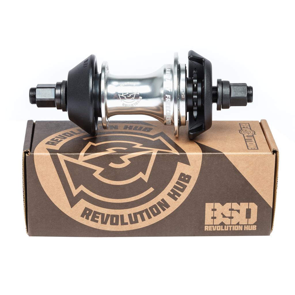 A silver BMX bike hub with a planetary clutch system sits on a cardboard box labeled "BSD Revolution Rear Freecoaster Hub" featuring the iconic logo.