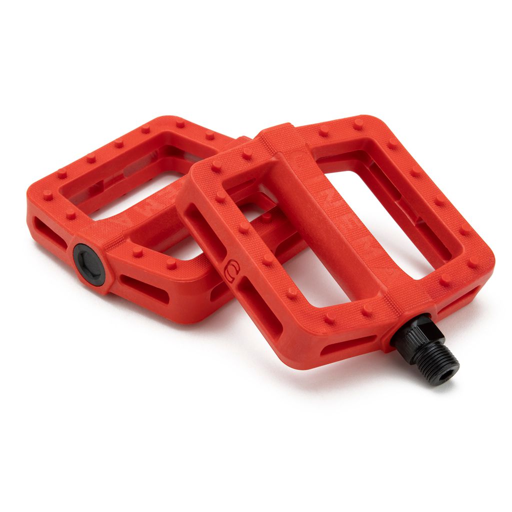 Displayed against a white background are two red Cinema Tilt Pedals, each featuring textured surfaces and black axle connectors. Their zero offset design and traction pins provide a secure grip while riding.