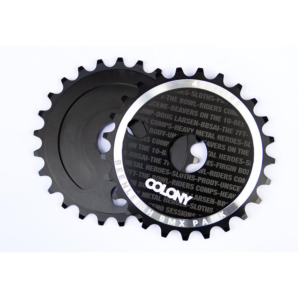Two overlapping black bicycle sprockets feature the "COLONY" logo and BMX text on top. This limited edition Colony Beenleigh 40 Years CD Sprocket 25T commemorates the Beenleigh Skatepark's four-decade legacy.