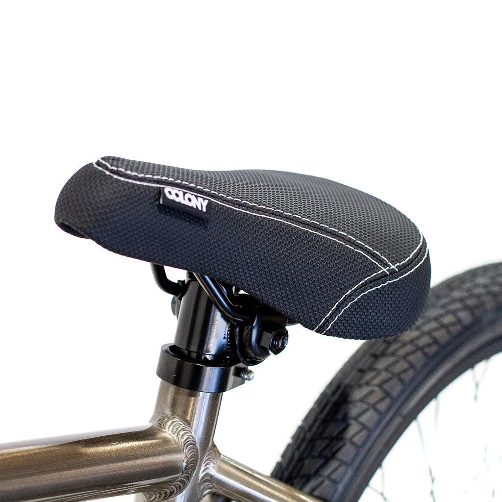 Close-up of a black, textured bicycle seat with white stitching on the lightweight alloy frame of the Colony Horizon 20 Inch Bike, showing part of the rear wheel and tire.