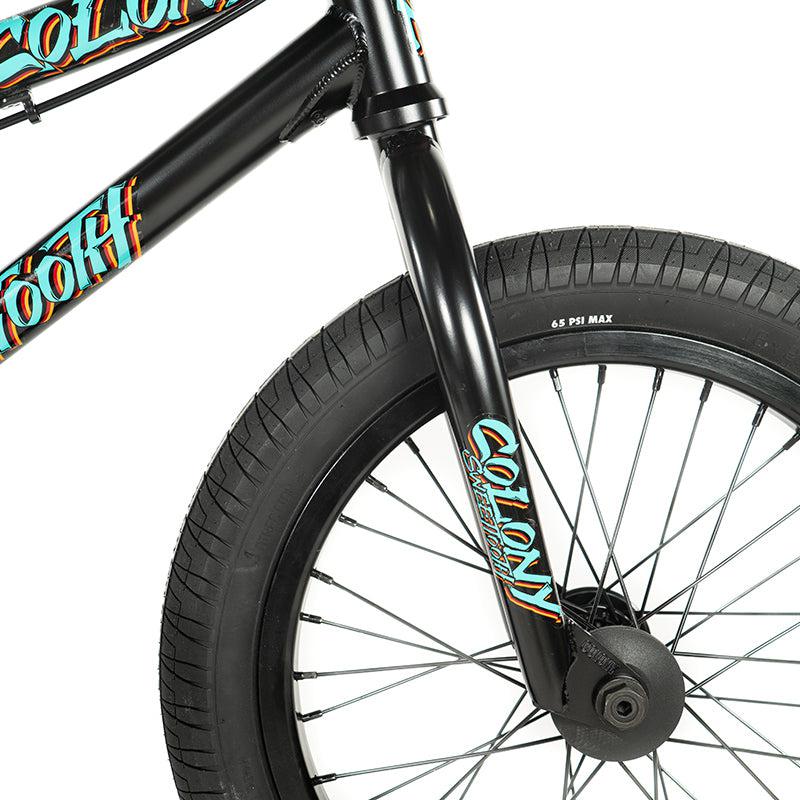 Close-up of the front wheel and fork of the black Colony Sweet Tooth Pro Elite 16 Inch BMX bike, showcasing colorful branding and a tire pressure rating of 65 PSI Max. The vibrant design enhances its high performance.