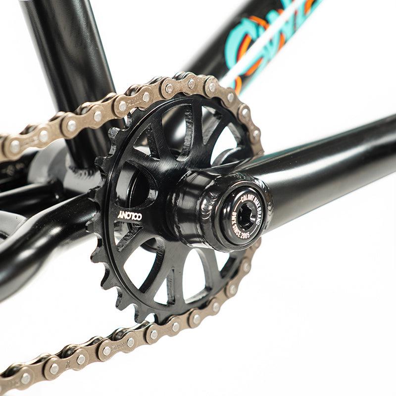 Close-up of a Colony Sweet Tooth Pro Elite 18 Inch BMX bike's chain and sprocket on a black frame, highlighting the intricate mechanics and streamlined design typical of Colony BMX craftsmanship.