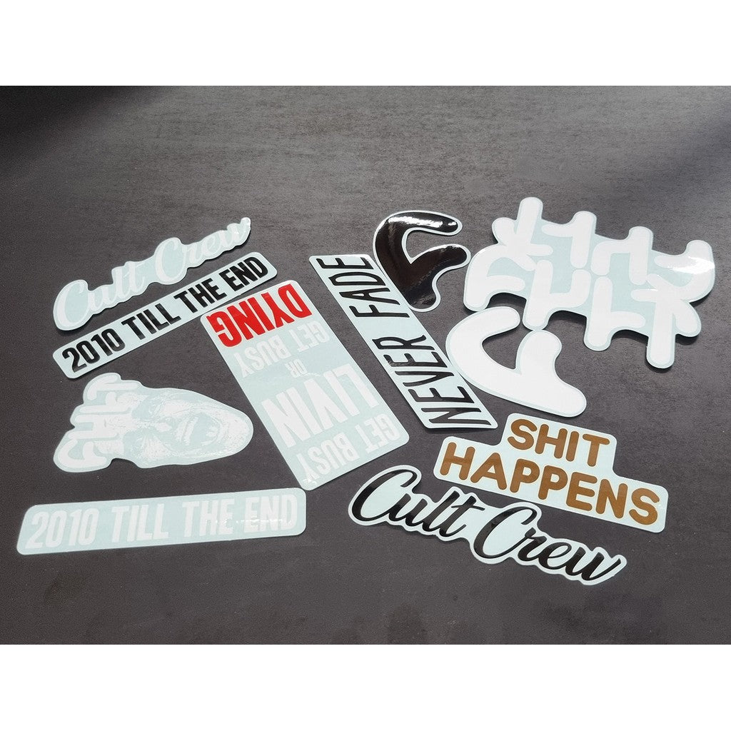 The Cult 11 Sticker Pack is displayed on a gray surface, featuring vibrant stickers with bold phrases such as "Cult Crew" and "Never Fade," capturing the essence of the Cult Brand BMX spirit with expressions like "Shit Happens" and "2010 Till the End.