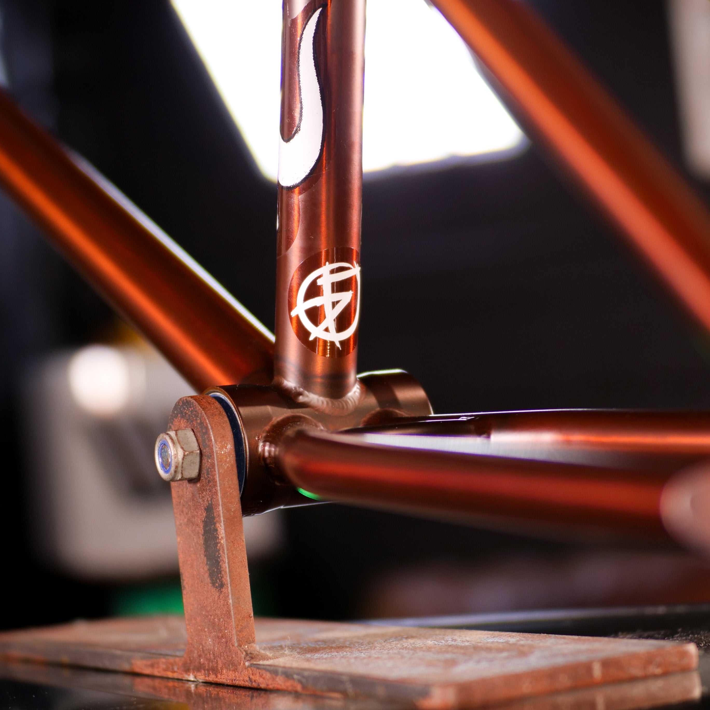 Close-up of a metallic brown Cult Dak Frame / Pat Freyne Signature BMX frame on a stand, featuring 100% cult classic tubing, precise welds, and two white decals.
