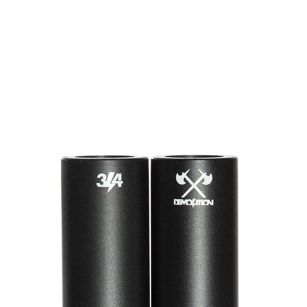 Two black cylindrical metal Demolition Axes Pegs stand upright—one marked "3/4," the other with a crossed-axes logo and "Demolition." Perfect BMX grind pegs for your next session.