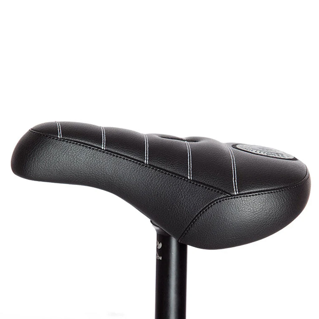 Close-up of the black Demolition Matt Cordova Seat (V2), showcasing its leatherette materials and white stitching, mounted on a black seat post with Pivotal Fat Cap Padding.