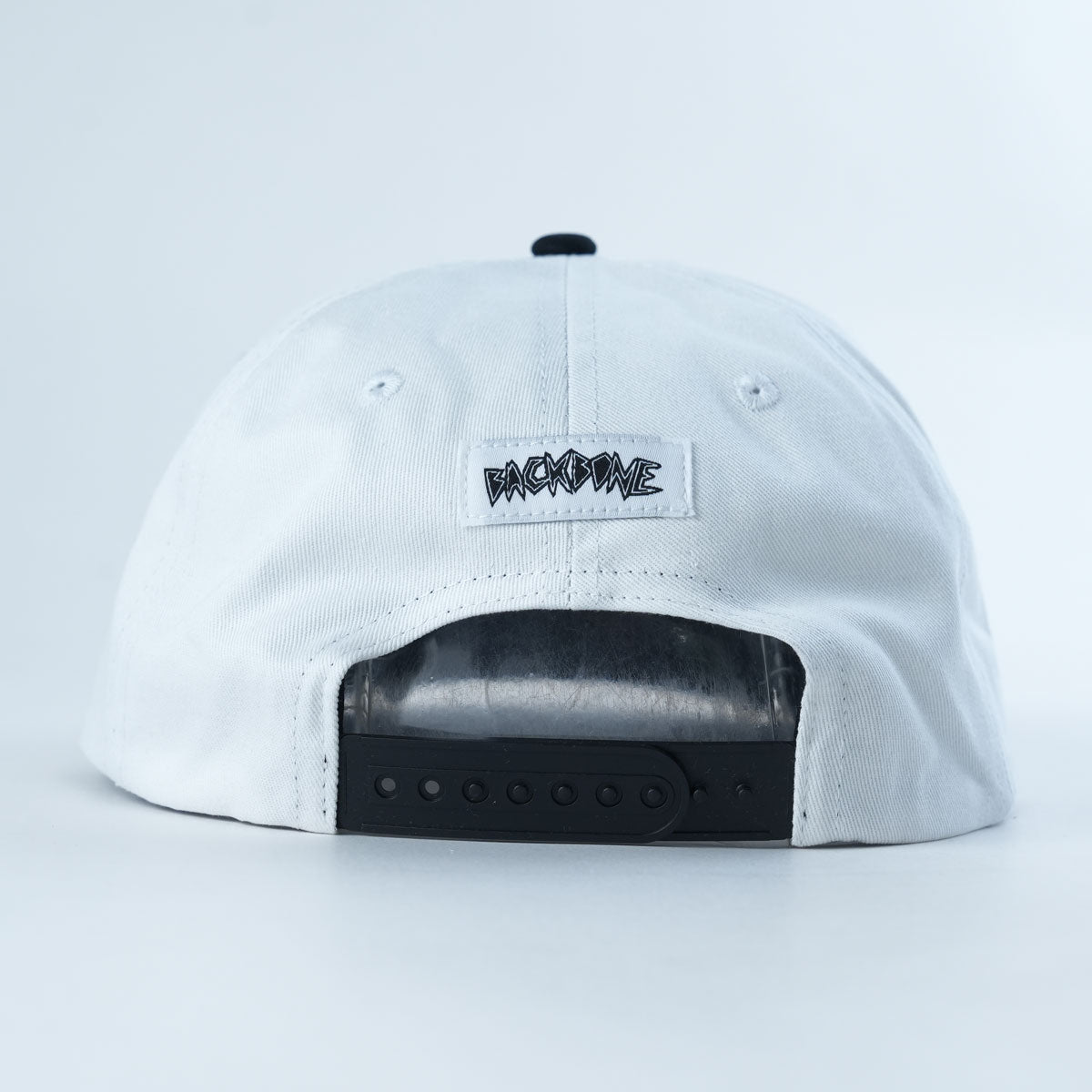 The Backbone Distance Snapback Hat is shown from the back, highlighting a black adjustable snapback closure and a small tag with stylized black “BACKBONE” text.