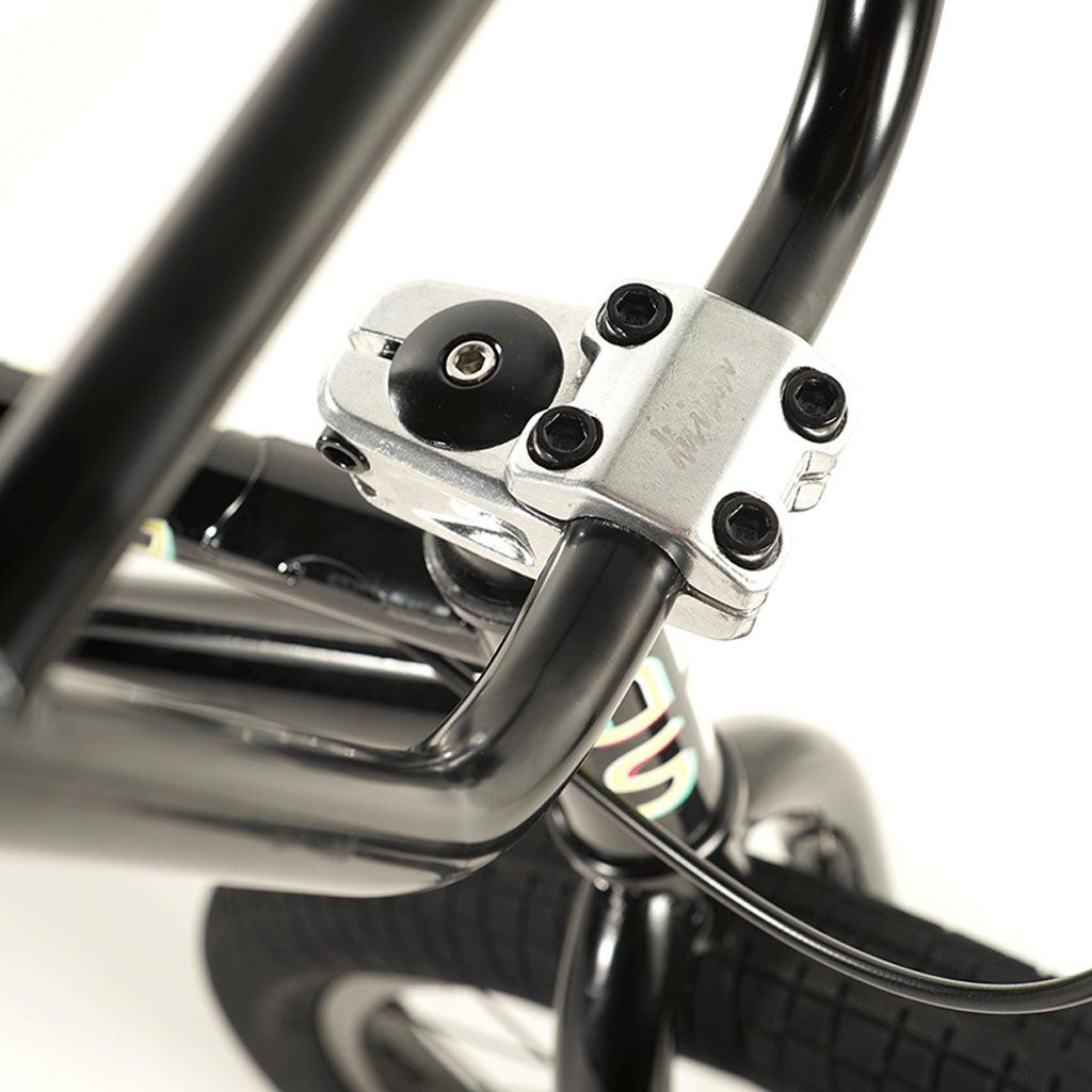 Close-up image of a black bicycle handlebar with a silver stem and four bolts secured in place. The front wheel of the Division Blitzer 20 Inch Bike, featuring a hi-tensile frame, is partially visible in the background.