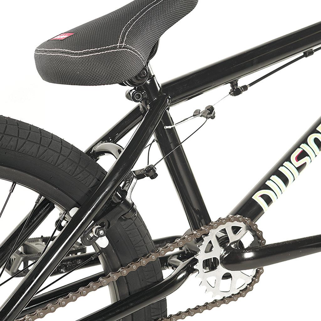 Close-up of a black Division Blitzer 20 Inch Bike focusing on the seat, pedal mechanism, and rear tire. The hi-tensile frame has "Division" written in white.