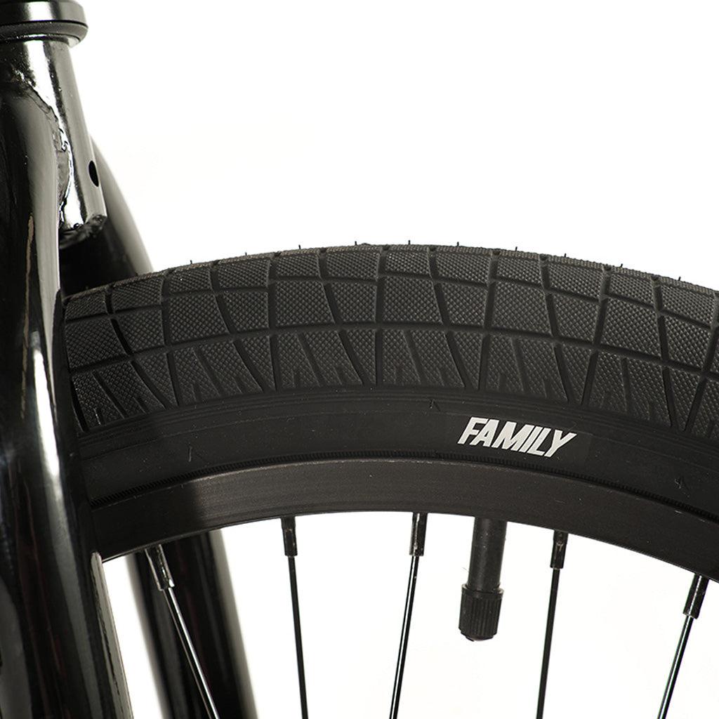 Close-up of the black wheel from a Division Blitzer 20 Inch Bike, showcasing the distinct tire tread and the word "FAMILY" on the sidewall. The image focuses on the BMX bike's 20-inch wheel and part of its hi-tensile frame.