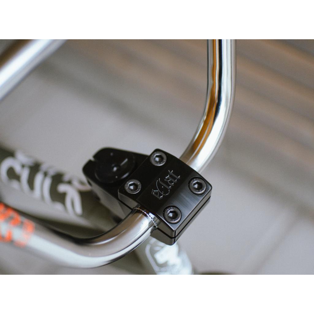 Close-up of a silver bicycle handlebar featuring the Eclat 1023 Stem in limited-edition black with bolts, showcasing mid-school styling and a textured side pattern.