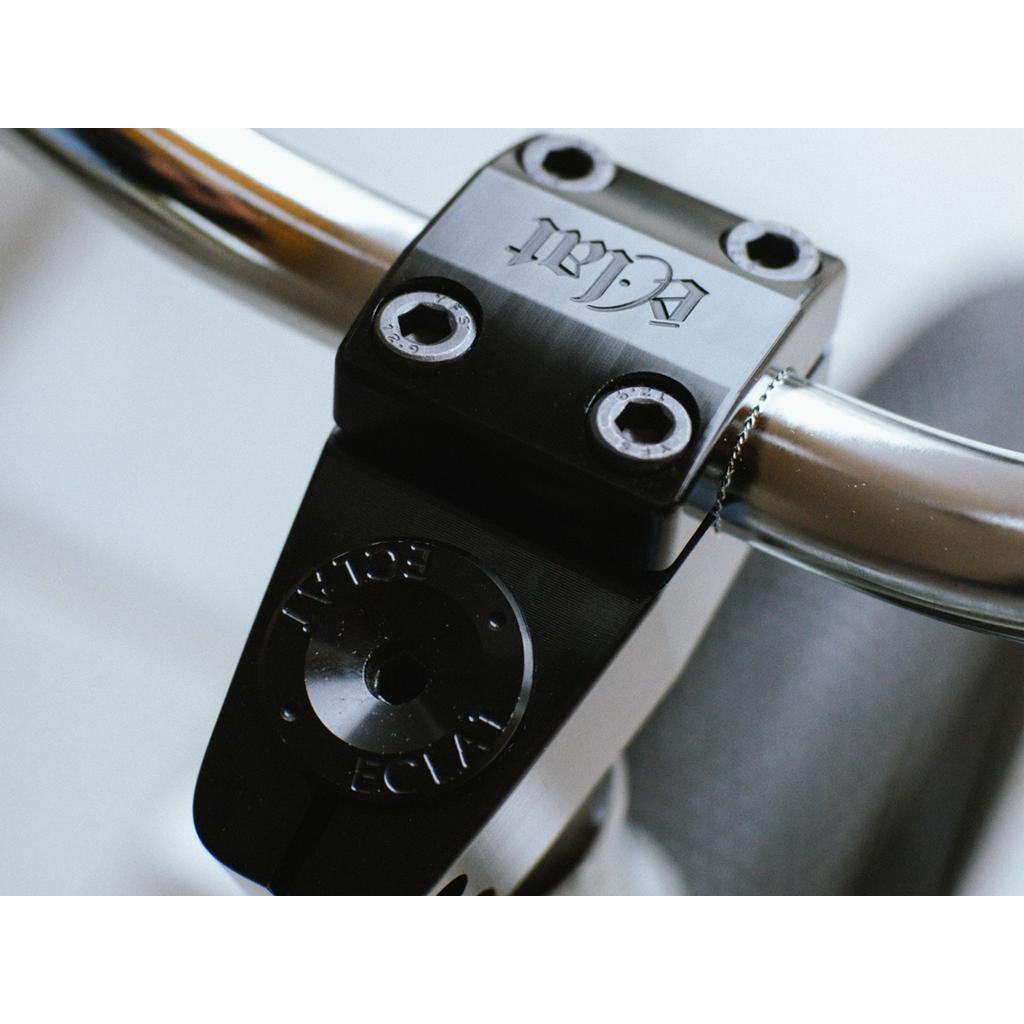 Close-up of a bicycle handlebar featuring the CNC machined Eclat 1023 Stem, a limited-edition model secured by four bolts. The engraved branding shines on the sleek metal, showcasing mid-school styling charm.