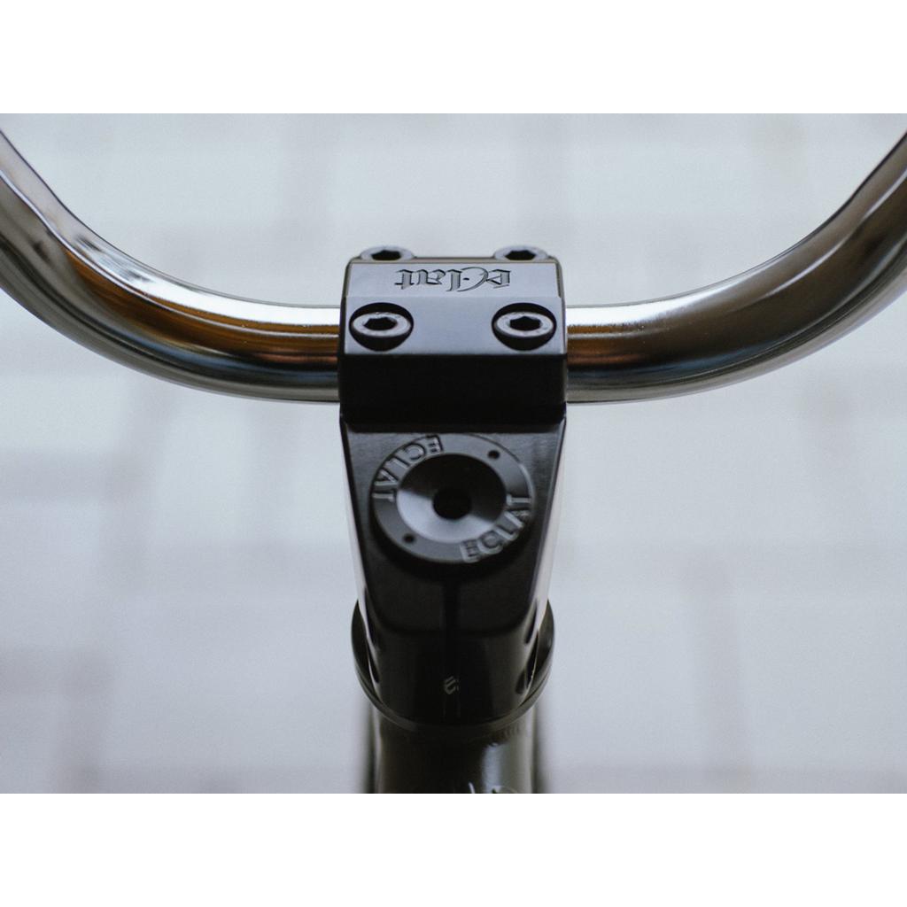Close-up of a bicycle handlebar with the CNC-machined, limited-edition Eclat 1023 Stem featuring classic mid-school styling. The brand name is embossed on the cap, and four visible bolts secure the stylish setup against an artfully blurred background.