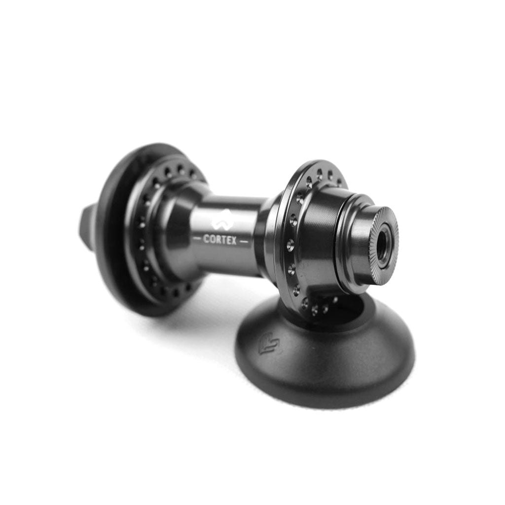 The Eclat Cortex/Seismic/Dynamic Nylon Front Hub Guard is a black hub with "Cortex" branding, multiple spoke holes, dual-sided flanges, and a central spindle. It includes an axle for improved stability and performance.