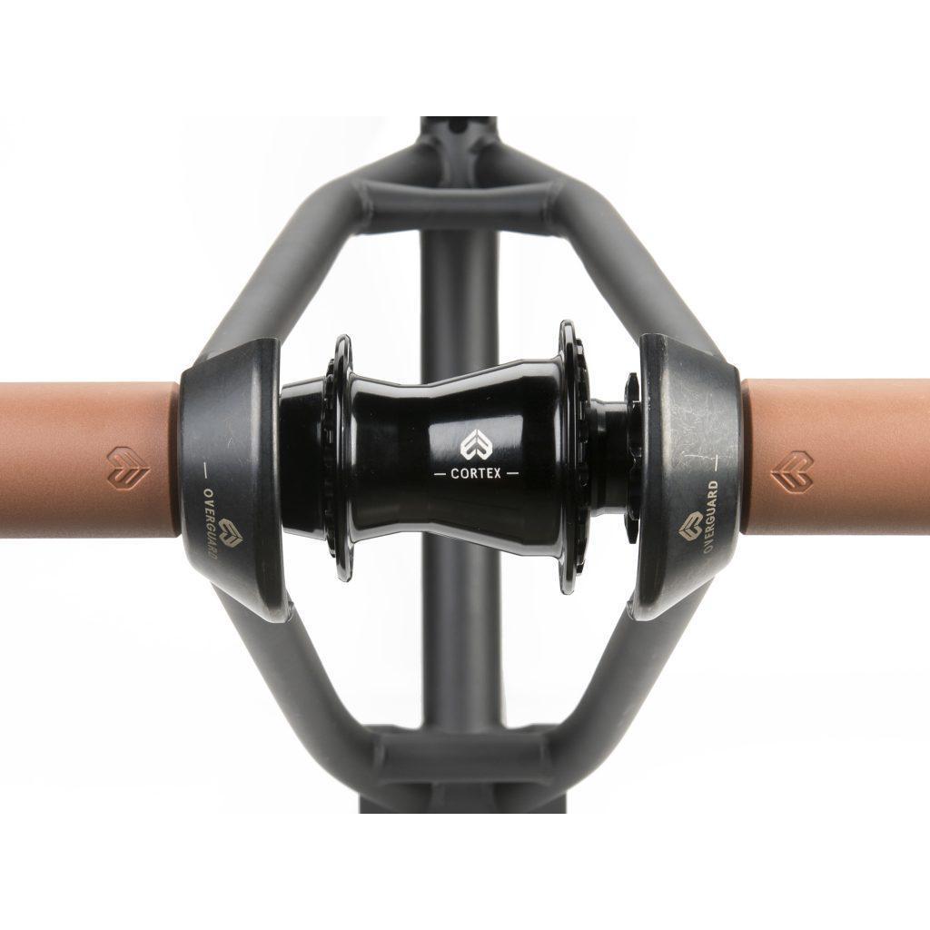 Close-up of the Cortex brand part on a bicycle handlebar, made from durable chromoly steel. The handlebars are brown with black connecting components, featuring the Eclat Overguard Steel Universal 14mm Hub Guard.