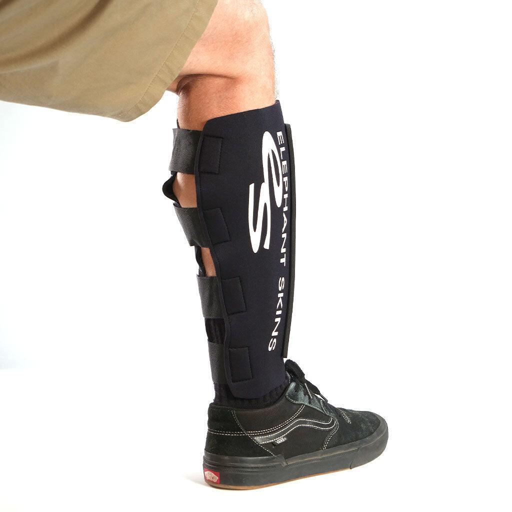 A person wears Elephant Skins Shin Pads (Pair)—lightweight black protective gear labeled "ELEPHANT SKINS," ideal for riding—along with black sneakers and khaki shorts.