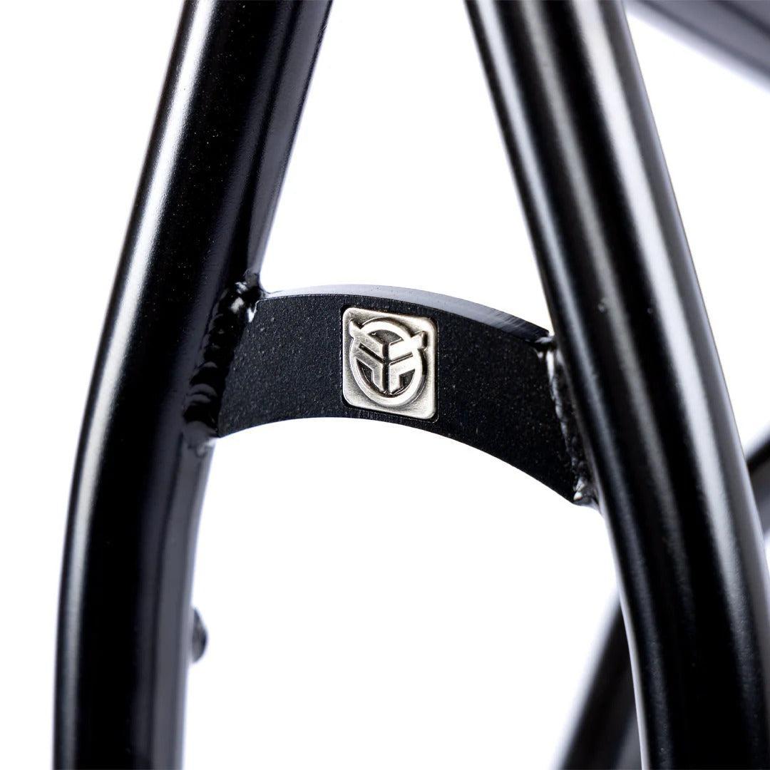 Close-up of the Federal Team ICS2 Frame in black, made from 4130 Chromoly tubing, featuring a silver badge with a stylized logo on the cross bracing—engineered for technical street riding.