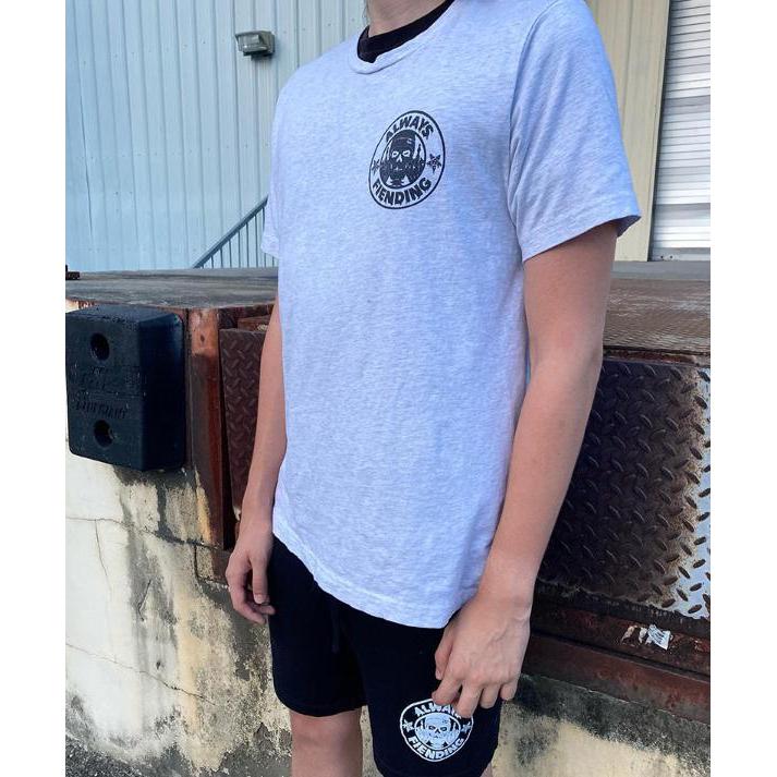 A person wearing a Fiend Always Fiending Shirt (Ash) and black shorts stands near a building with a metal dock plate outdoors.