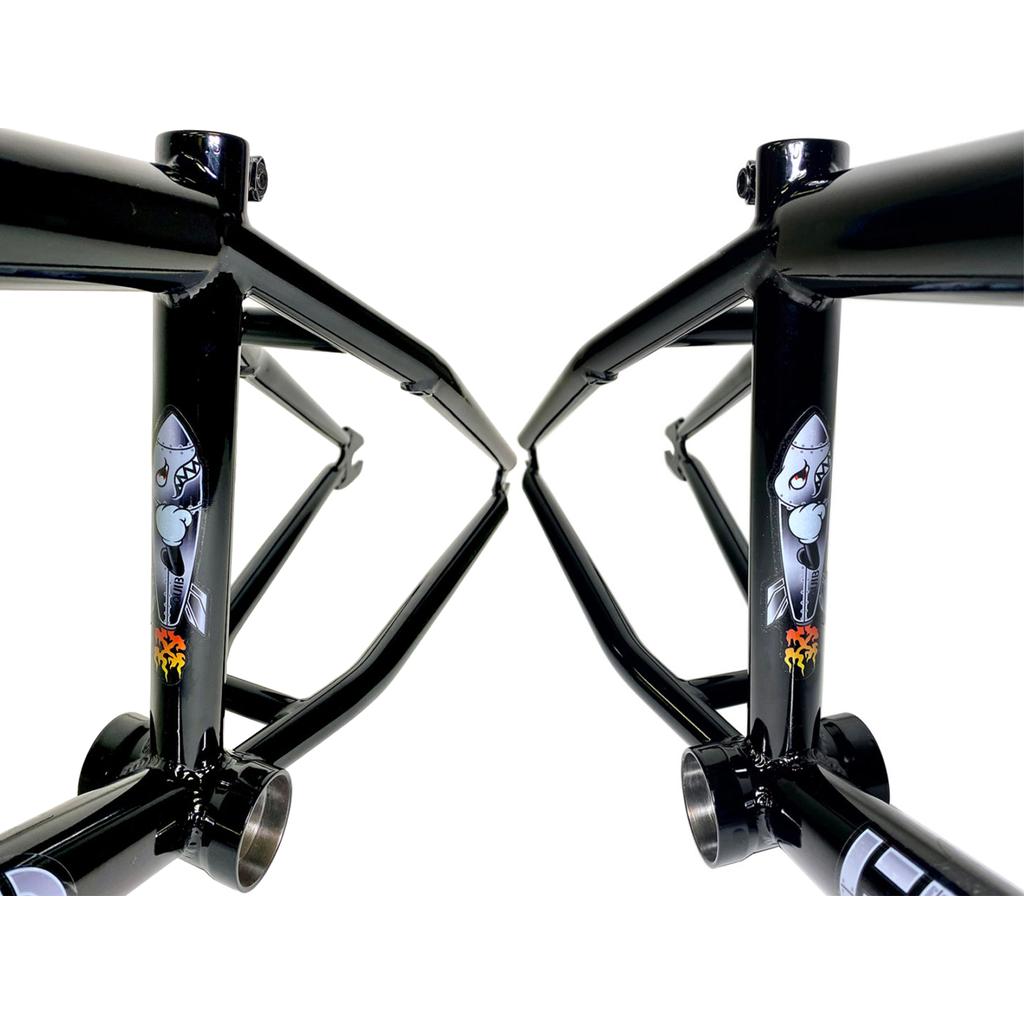 Two Fit Bike Co Squib 20 Inch Frames, crafted from sleek black chromoly for optimal performance, feature a striking shark decal with flames near the bottom bracket. Perfectly suited for trail geometry, they stand side by side against a pristine white background.