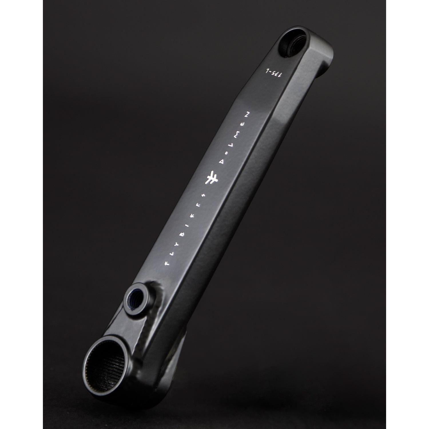 A black Fly Bikes Dolmen 24 crank arm, crafted from CNC machined 4130 Chromoly, is shown on a dark background with white markings and text highlighting its precision and durability.