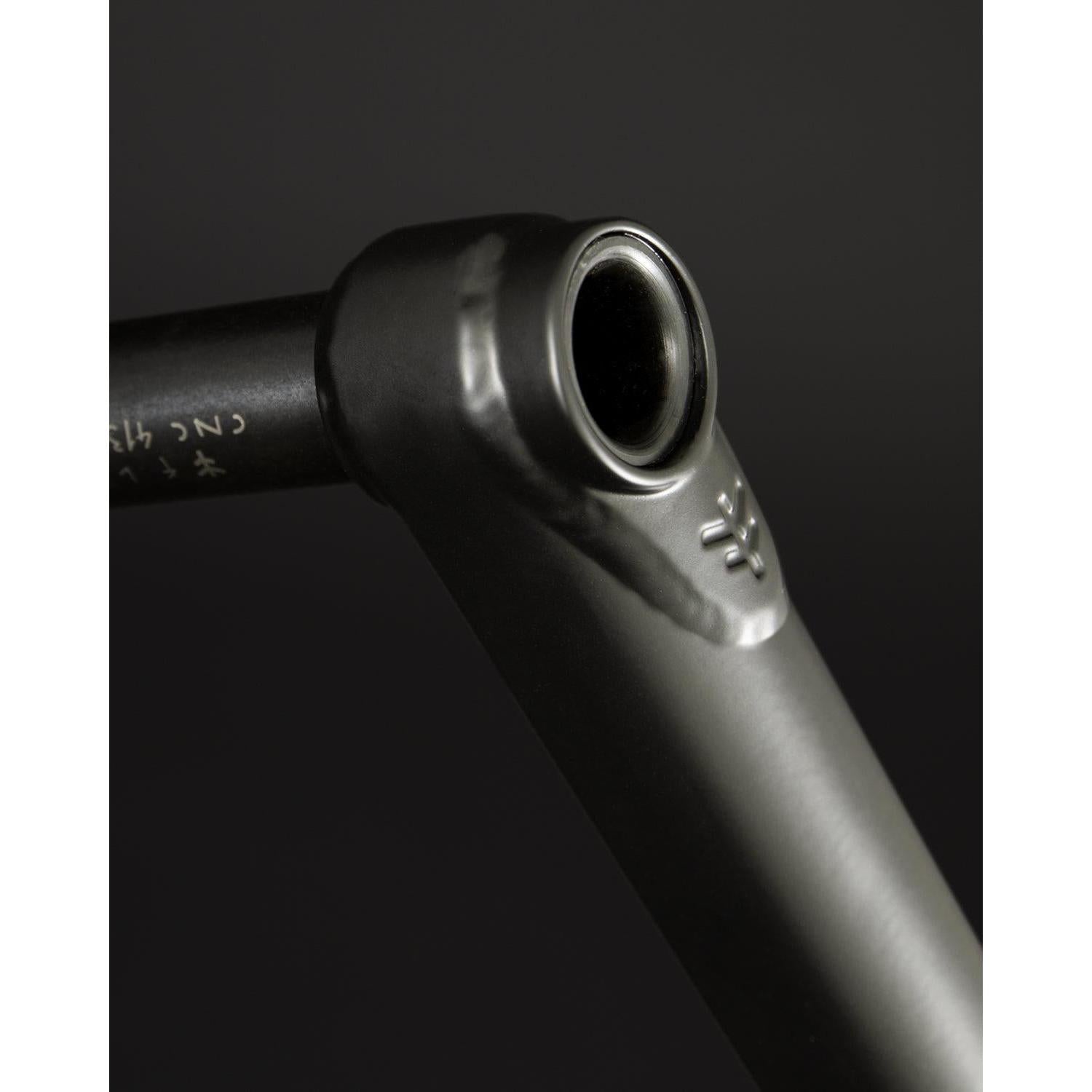 A close-up showcases the Fly Bikes Dolmen 24 Cranks, a sleek black metal part, likely CNC machined from 4130 Chromoly. It features a cylindrical opening and detailed engraved markings set against a dark background.