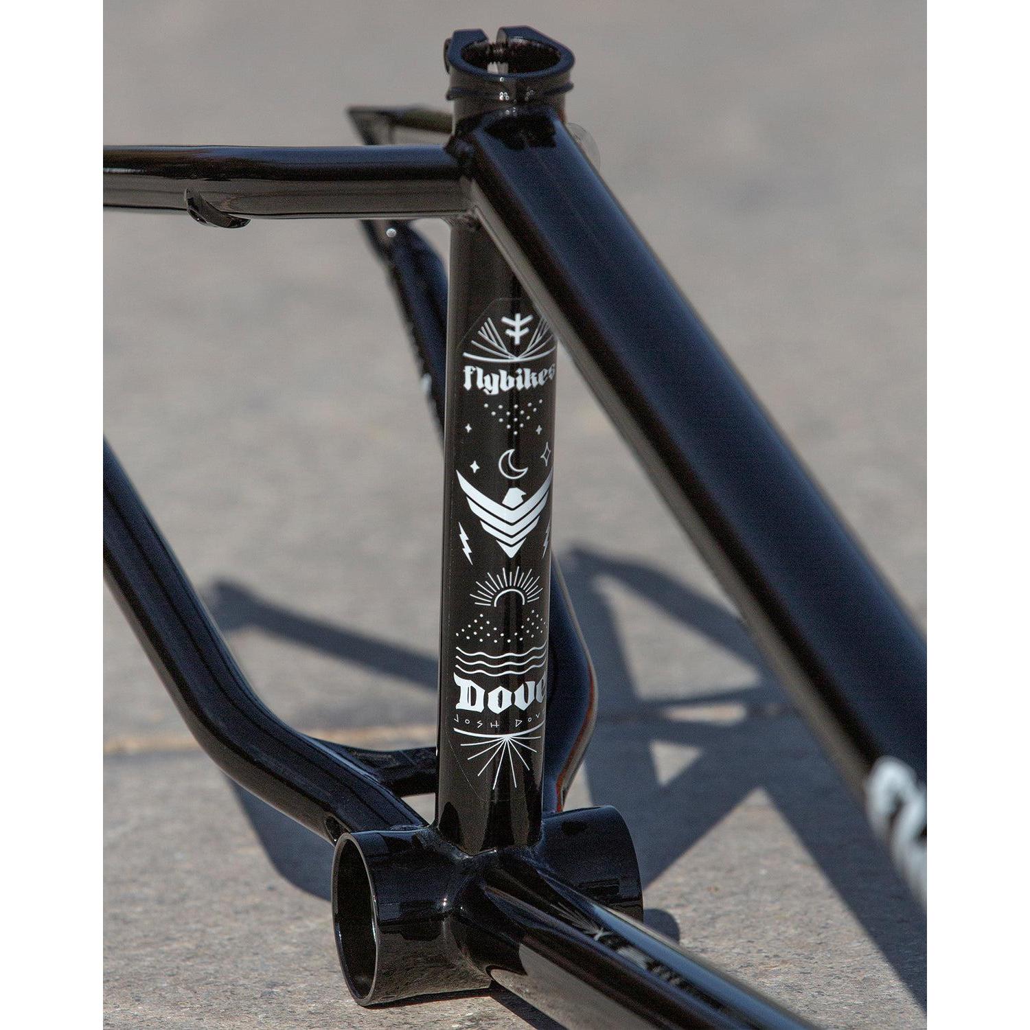 Close-up of the black Fly Bikes Dove 13.2 Frame on concrete, adorned with white graphics featuring symbols and text. Perfect for park riding, its sleek design blends style and performance seamlessly.