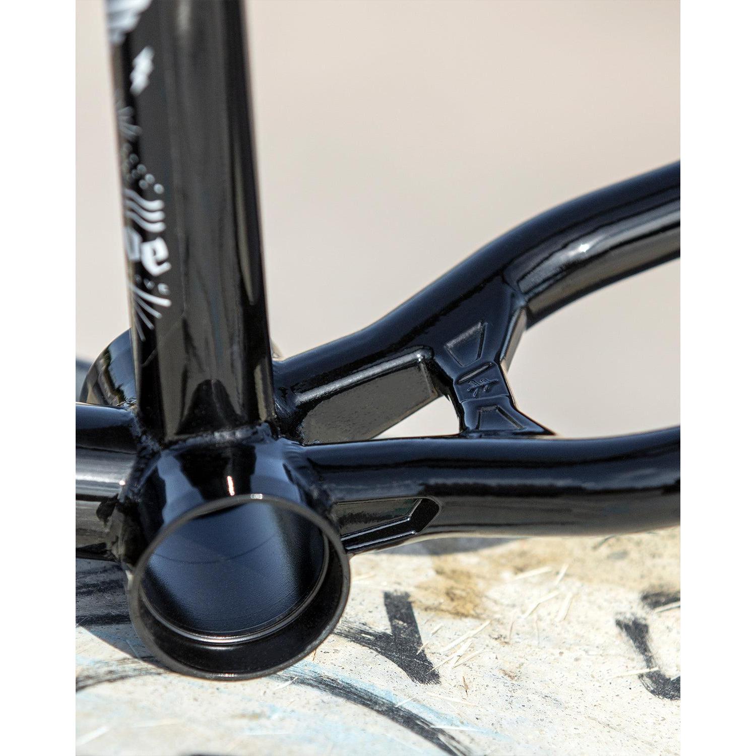 Close-up of a Fly Bikes Dove 13.6 BMX frame (Josh Dove Signature) in black, highlighting the bottom bracket and chainstay junction on a concrete surface, showcasing its sleek geometry.