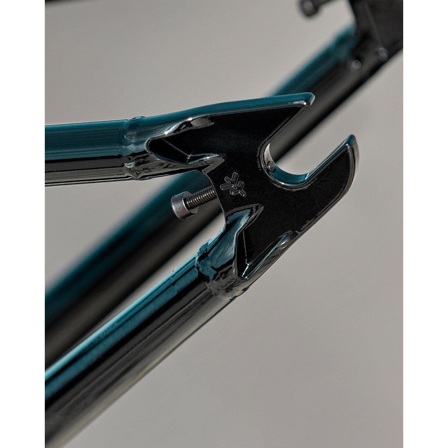 Close-up of the Fly Bikes Dove 13.6 Frame (Josh Dove Signature) in black and teal, featuring a bolt and distinct metalwork on a neutral background, highlighting its fine geometry.