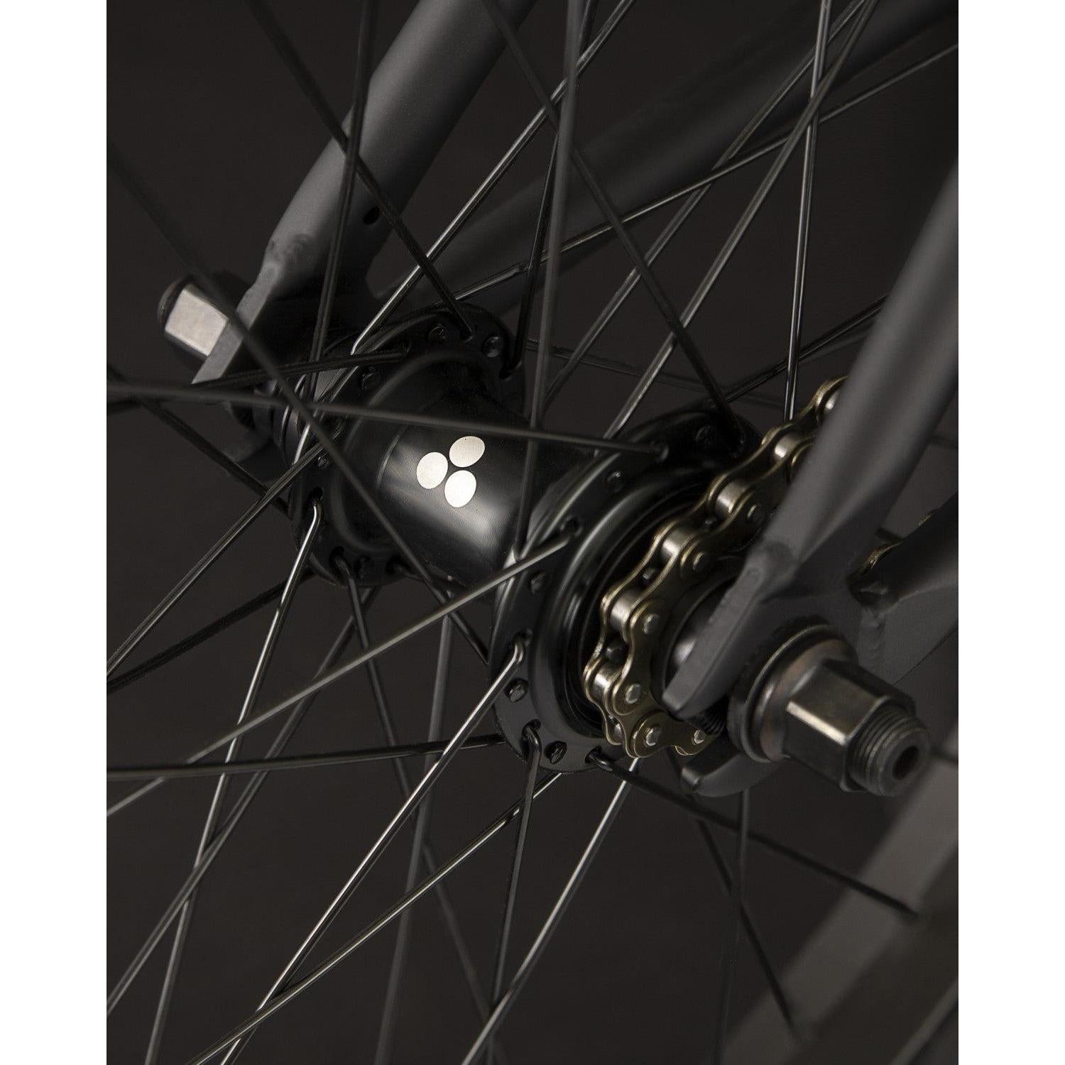 Close-up of the Fly Bikes Electron 20 Inch Bike wheel hub featuring the iconic three-dot logo, highlighting the durable Cr-Mo material, spokes, and chain mechanism in view.