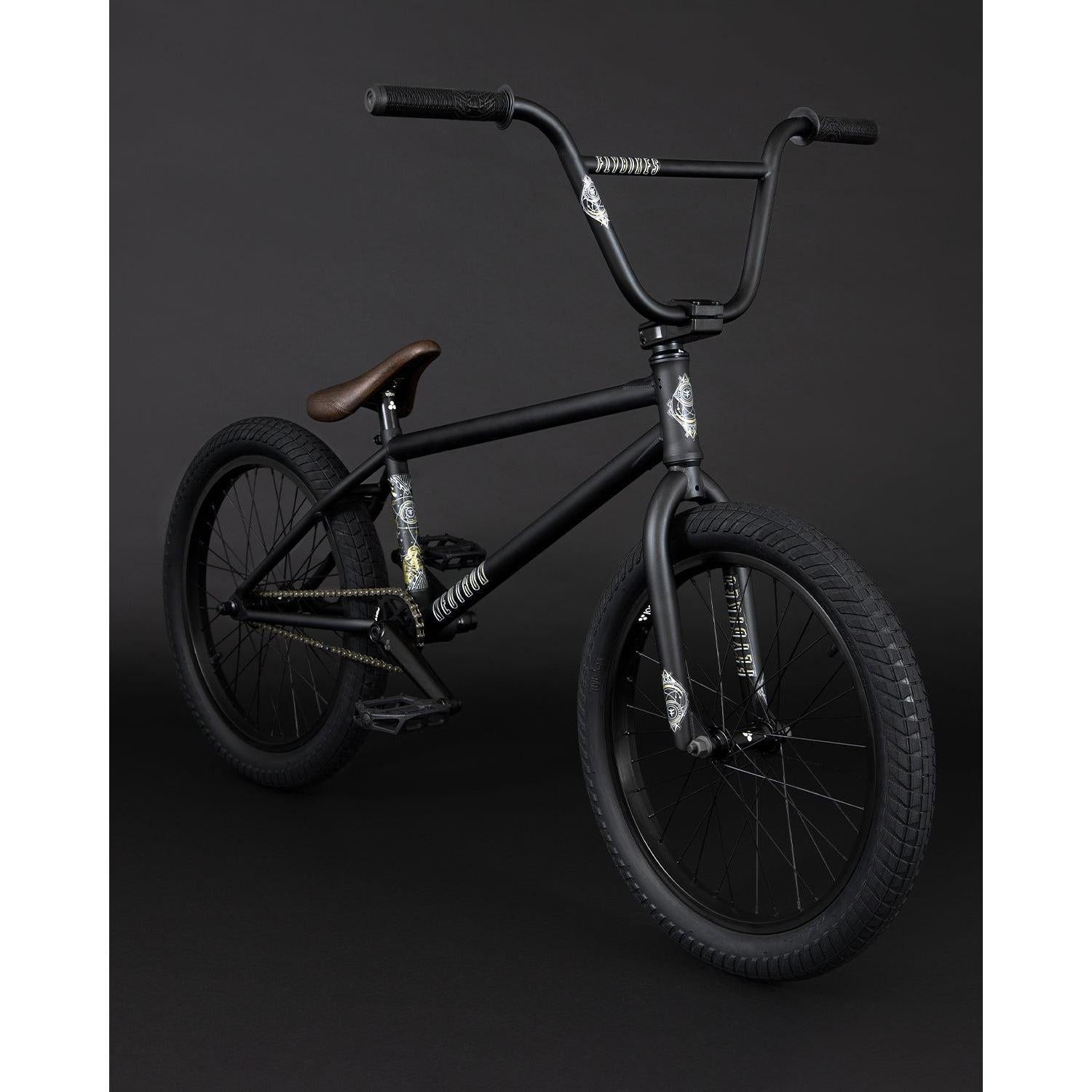 Introducing the Fly Bikes Neutron 20 Inch Bike, a sleek black BMX with a CrMo frame, adorned with graphic designs and complemented by a brown seat, all strikingly contrasted against a dark background.