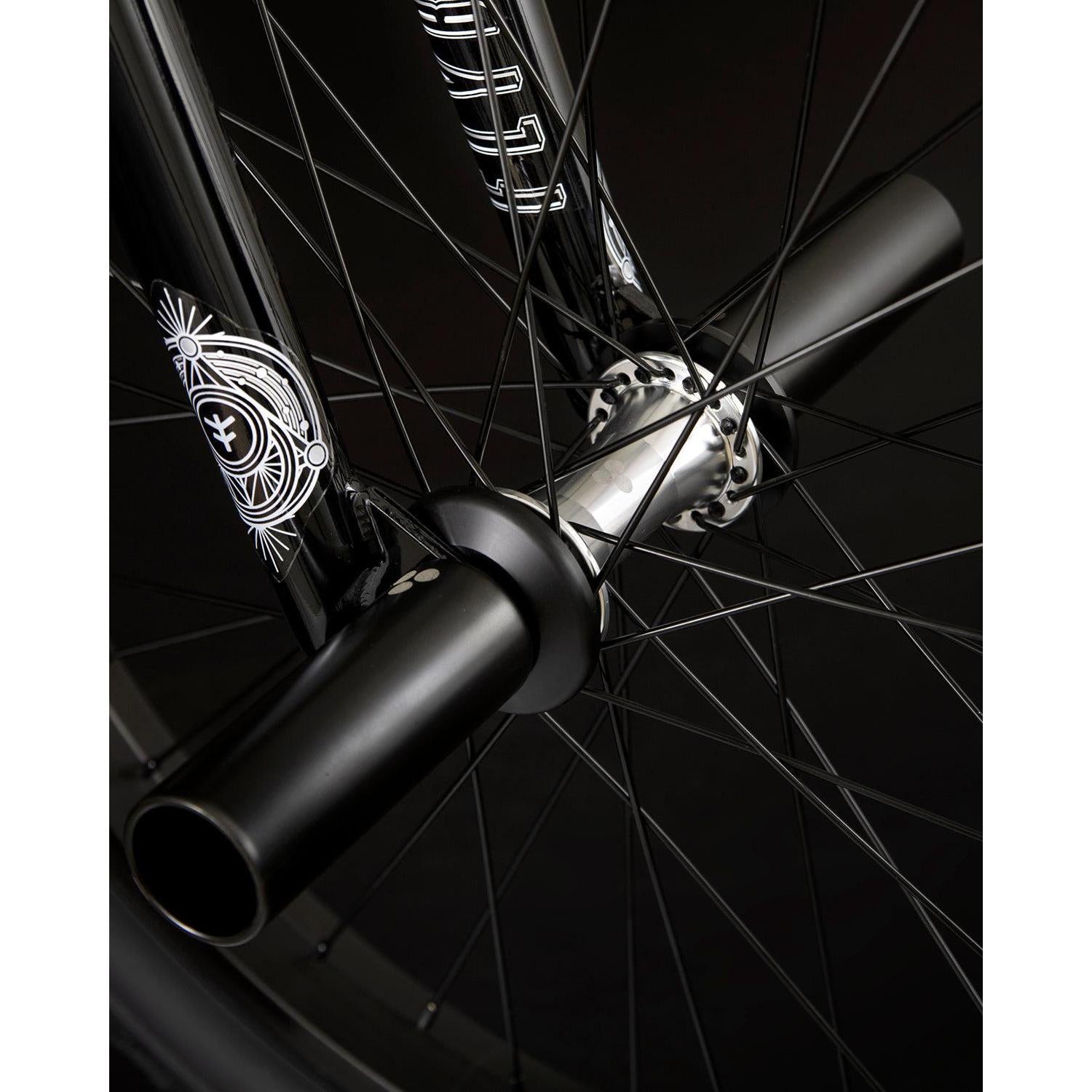 Close-up view of the Fly Bikes Proton FC 20 Inch Bike's black wheel, featuring an intricate spoke design, sealed hubs, and axle pegs, set against a dark background.