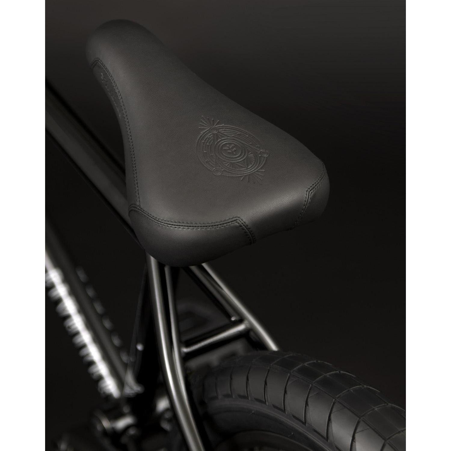 Close-up of the black bicycle seat with a subtle embossed design, mounted on the sleek Fly Bikes Proton FC 20 Inch BMX bike featuring a sturdy CrMo frame against a dark background.