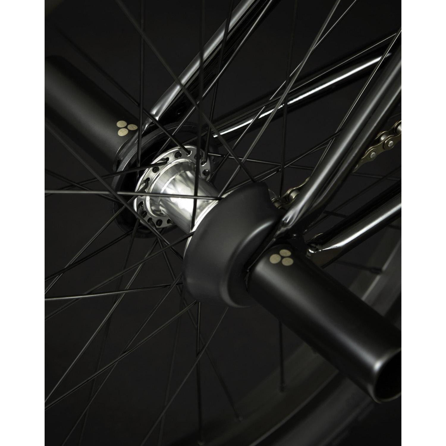 Close-up of the Fly Bikes Proton FC 20 Inch Bike's wheel, showcasing black spokes with a silver hub and black pegs on the axle. This durable configuration is complemented by its CrMo frame, providing a robust ride.