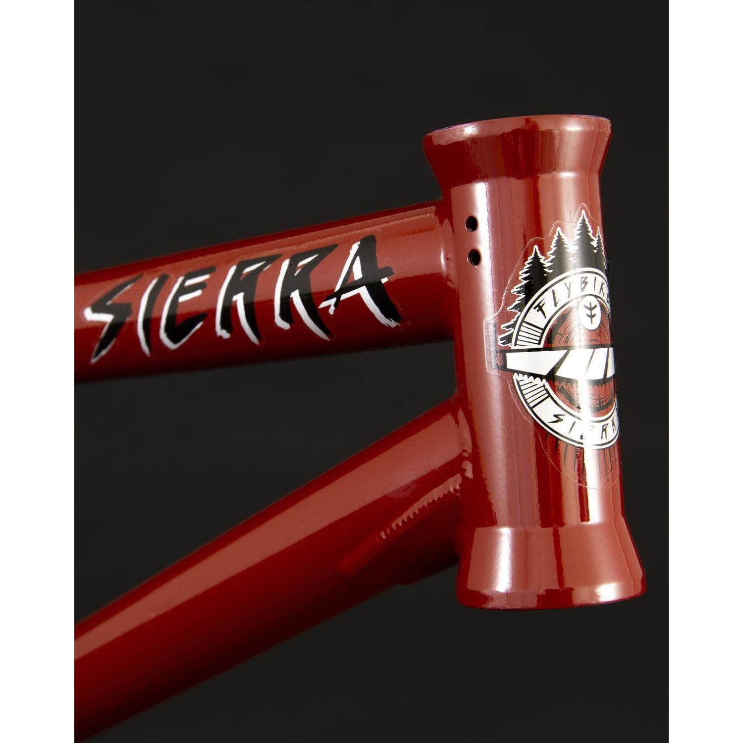Close-up of a Fly Bikes Sierra Frame in red, made from durable 4130 CrMo steel, featuring the word "Sierra" and an emblem with trees on a stylish black background.