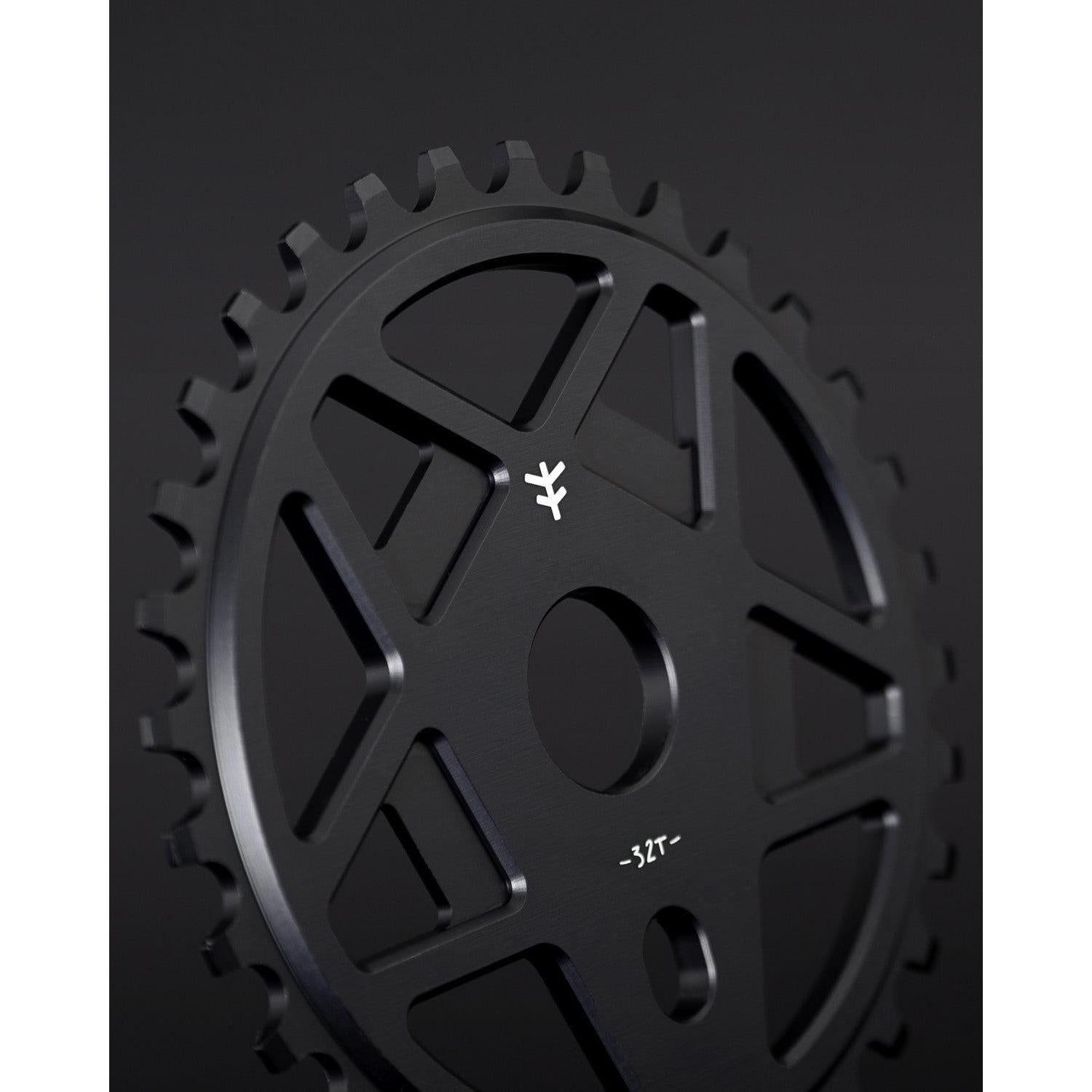 The Fly Bikes Tractor TT Sprocket is a black chainring made from durable 6061 T-6 Aluminum, featuring a minimalist design with cut-out sections and small white "32T" text beside an emblem inspired by Tractor TT's iconic sprocket style.