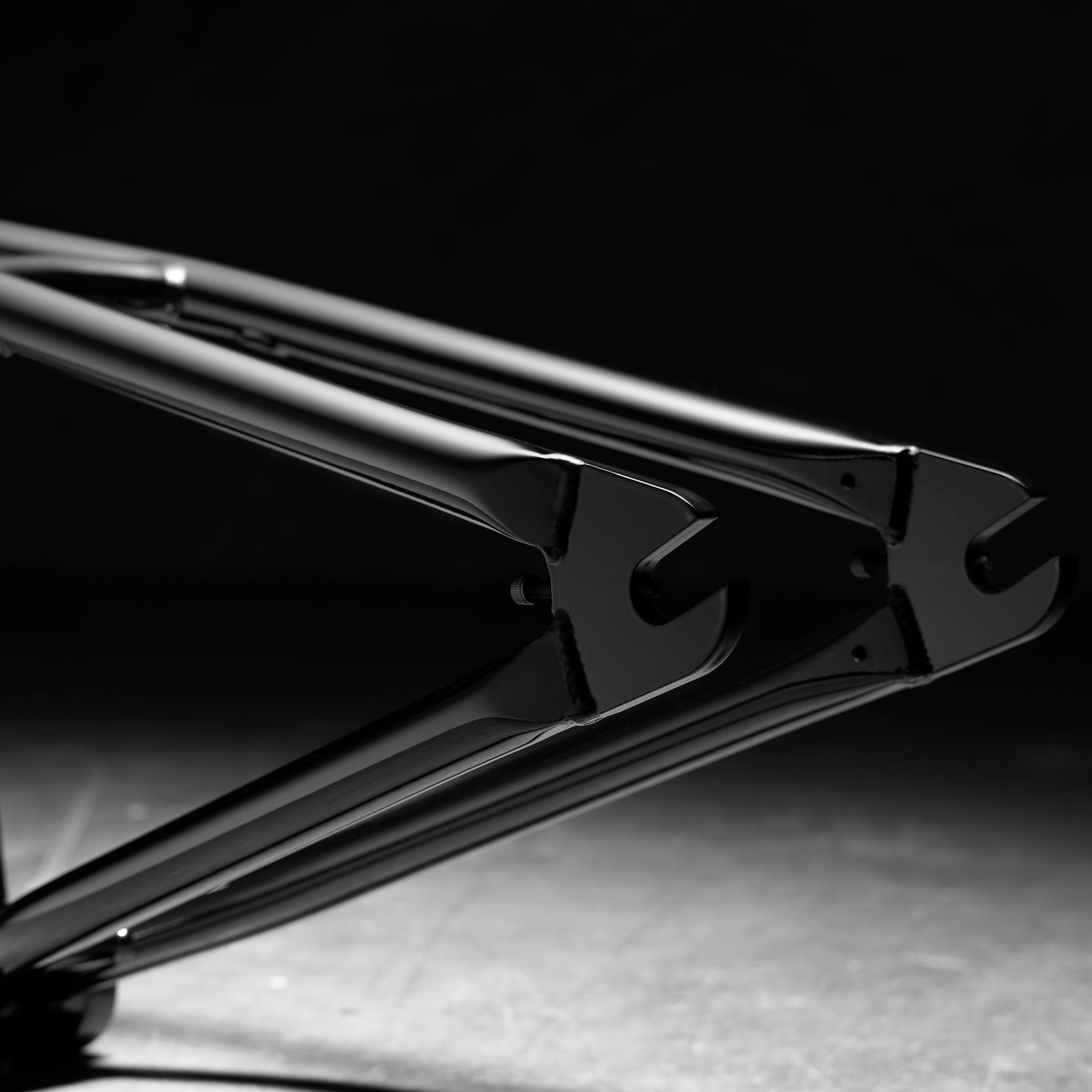 Close-up of the rear dropouts and chainstays on the Kink Prophet Frame, a black BMX frame made from chromoly tubing, set against a dark background with dramatic lighting.