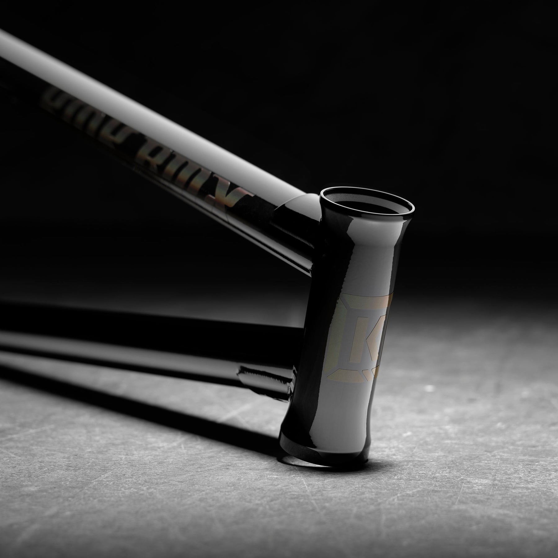 Close-up of the Kink Prophet Frame, a glossy black BMX frame featuring a prominent head tube and integrated chain tensioners, set against a dark, blurred background.