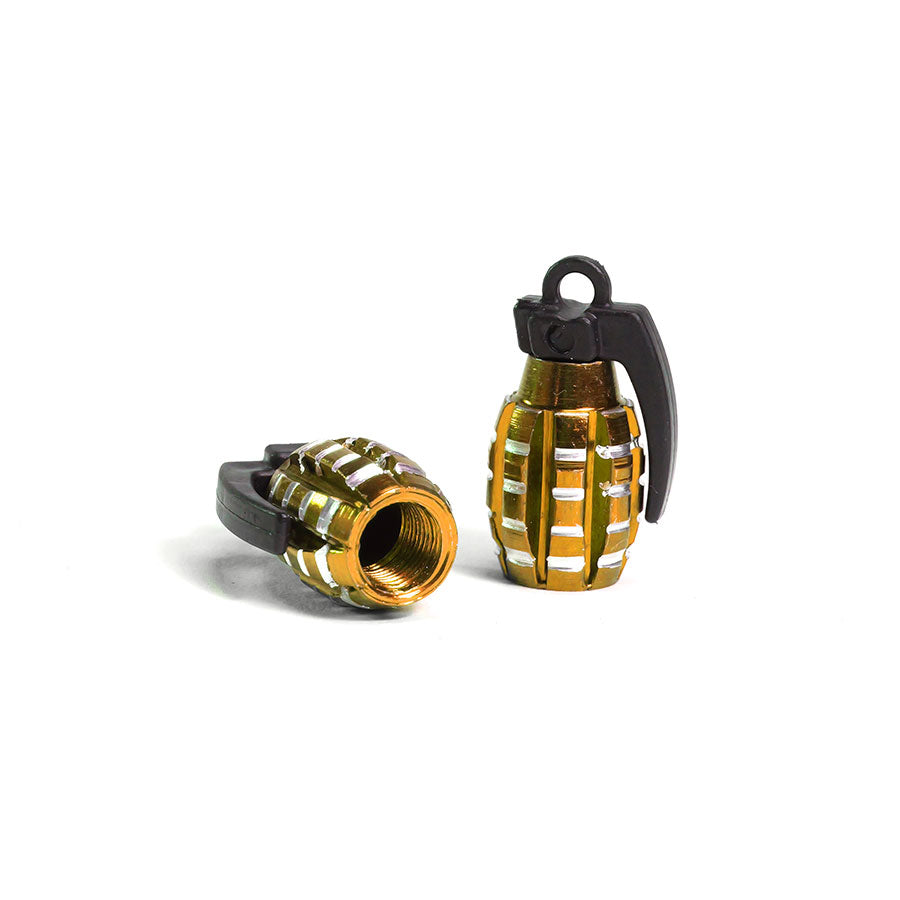 A pair of small, gold and black Grenade Valve Caps featuring a visible Schrader valve—one standing upright, the other lying down—displayed on a plain white background.