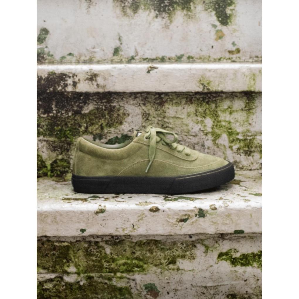 The Higher Crypt Suede Lace Up Shoes (Olive/Black) featuring a green suede upper and black sole with detailed grip are displayed on weathered, mossy white concrete stairs.