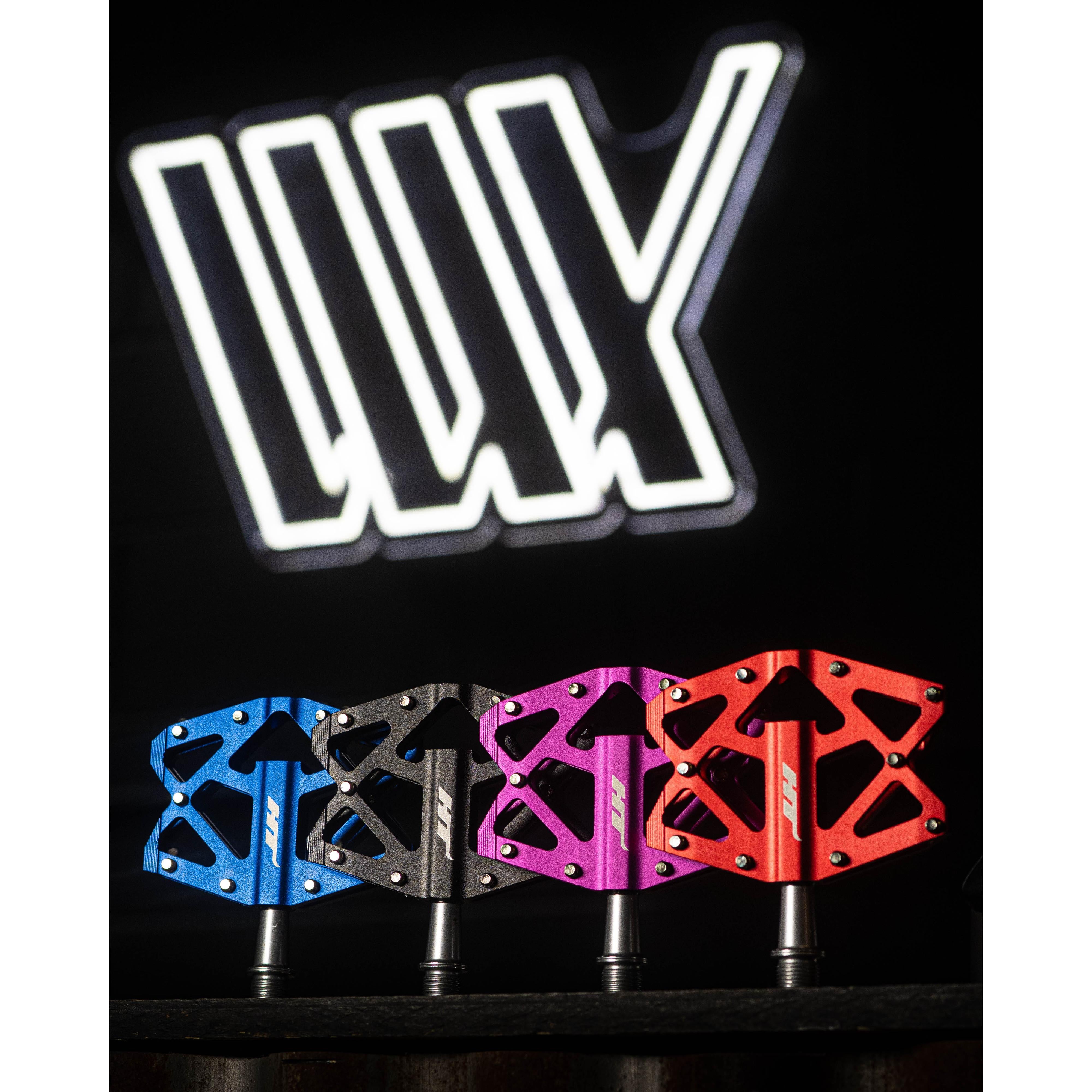 The HT AXO1A Nano Pedals in blue, black, pink, and red stand out against a dark backdrop with a white logo. Designed for lightweight performance, these pedals provide exceptional grip for cycling enthusiasts.