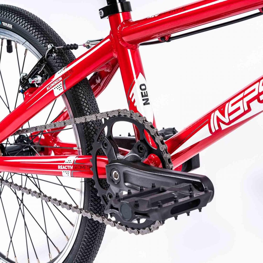 Close-up of a red Inspyre Neo Pro Bike race bike's rear wheel, chain, and gear mechanism.